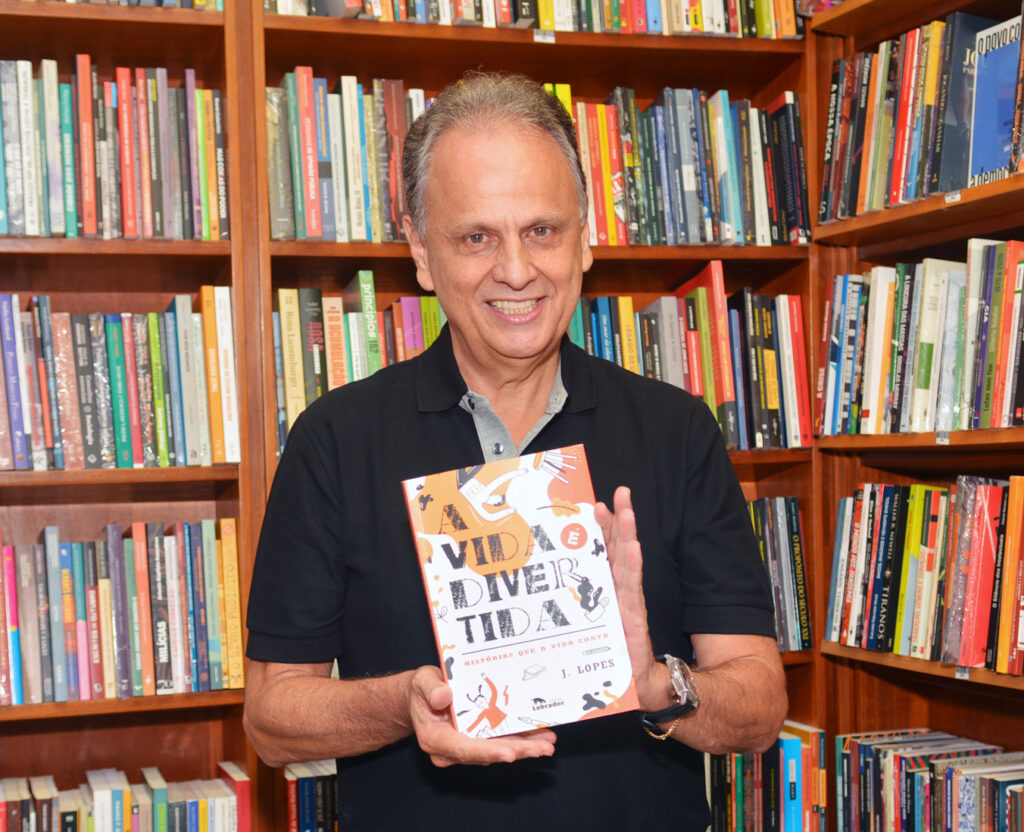 J. Lopes apresenta o livro A vida é divertida diante de uma estante